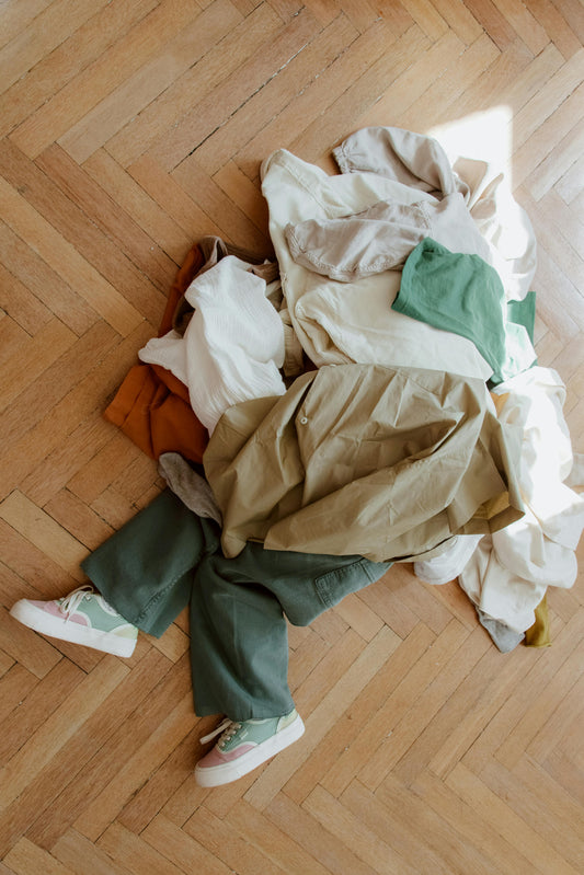 A mom and twoA child sits under a pile of gently used kids' clothes on the living room floor, that are ready donation or swapping.